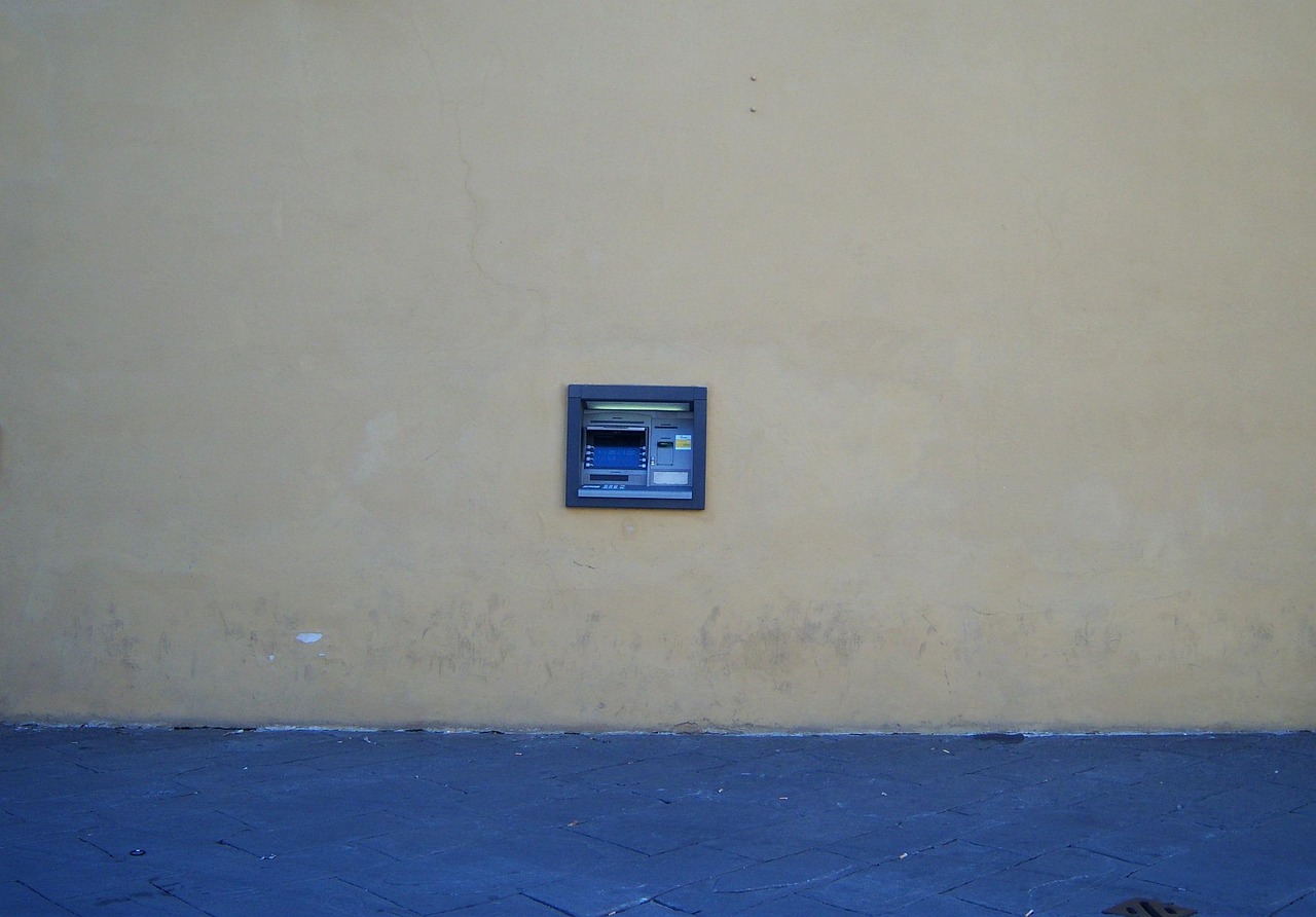 Immagine di un bancomat con avviso di sicurezza e POS in primo piano, simboli di allerta finanziaria.